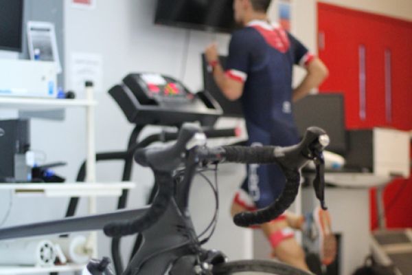 Atleta corriendo sobre una caminadora con instrumentos de medición en su cuerpo.