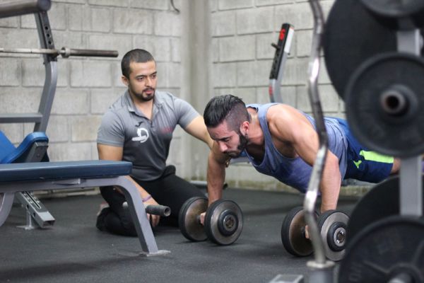 Un entrenador junto a su atleta supervisando ejercicio con pesas