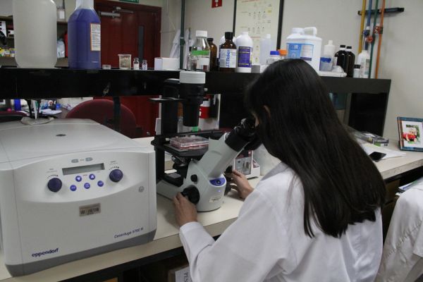 Una mujer realizando análisis mediante microscopio en el laboratorio de Virología